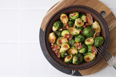 Photo of Delicious roasted Brussels sprouts and bacon in bowl on white table, top view. Space for text