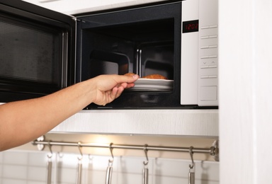 Young man putting plate with croissants in microwave oven, closeup