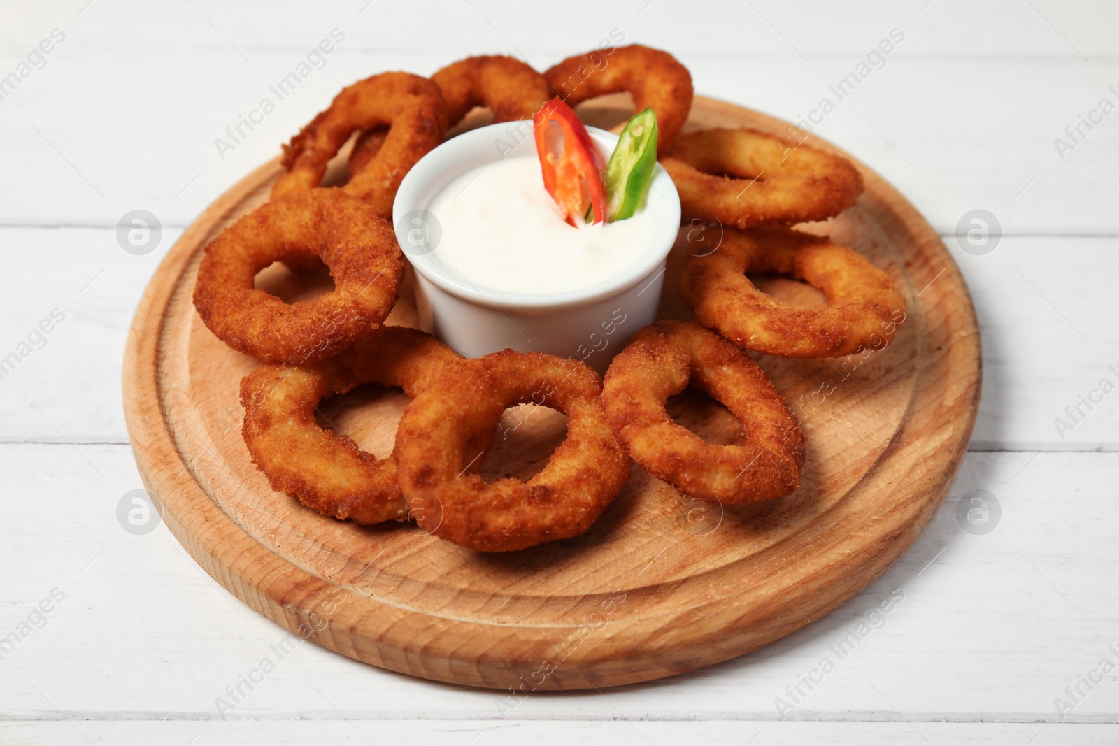 Photo of Wooden board with tasty onion rings and sauce on table