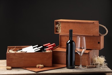 Boxes with wine bottles, corks and glass on wooden table against black background