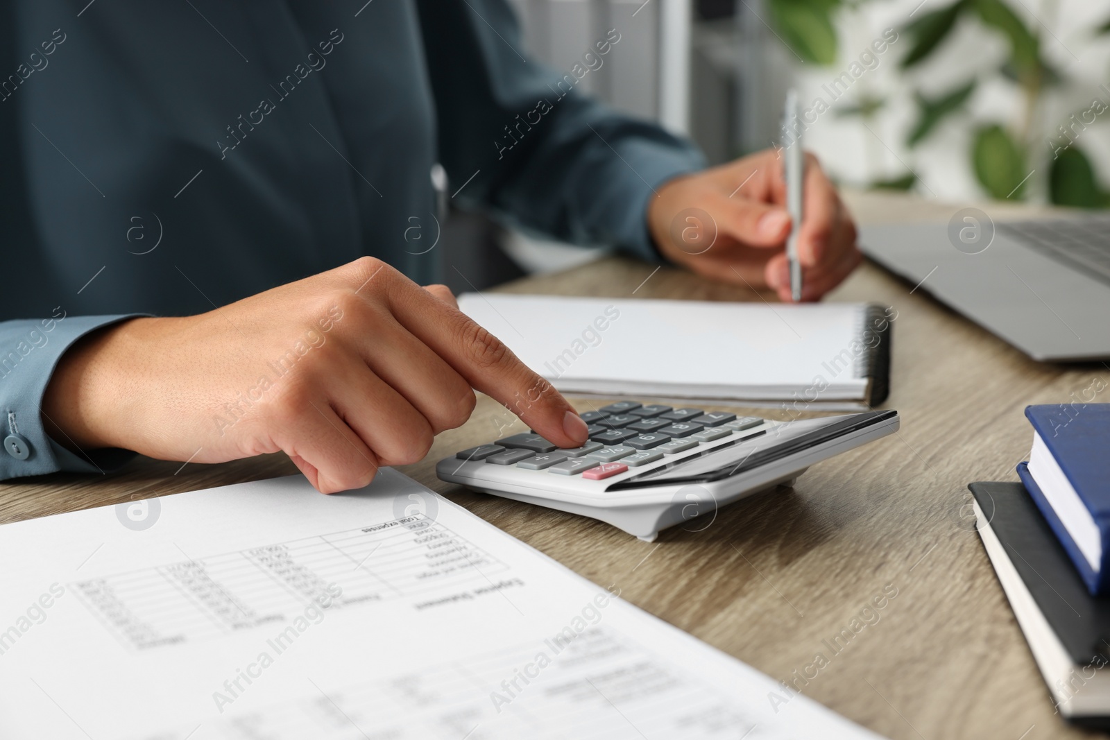 Photo of Woman using calculator while taking notes at wooden table, closeup