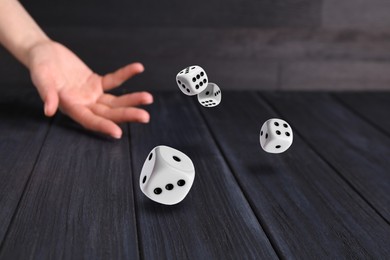 Image of Woman throwing white dice on black wooden table, closeup