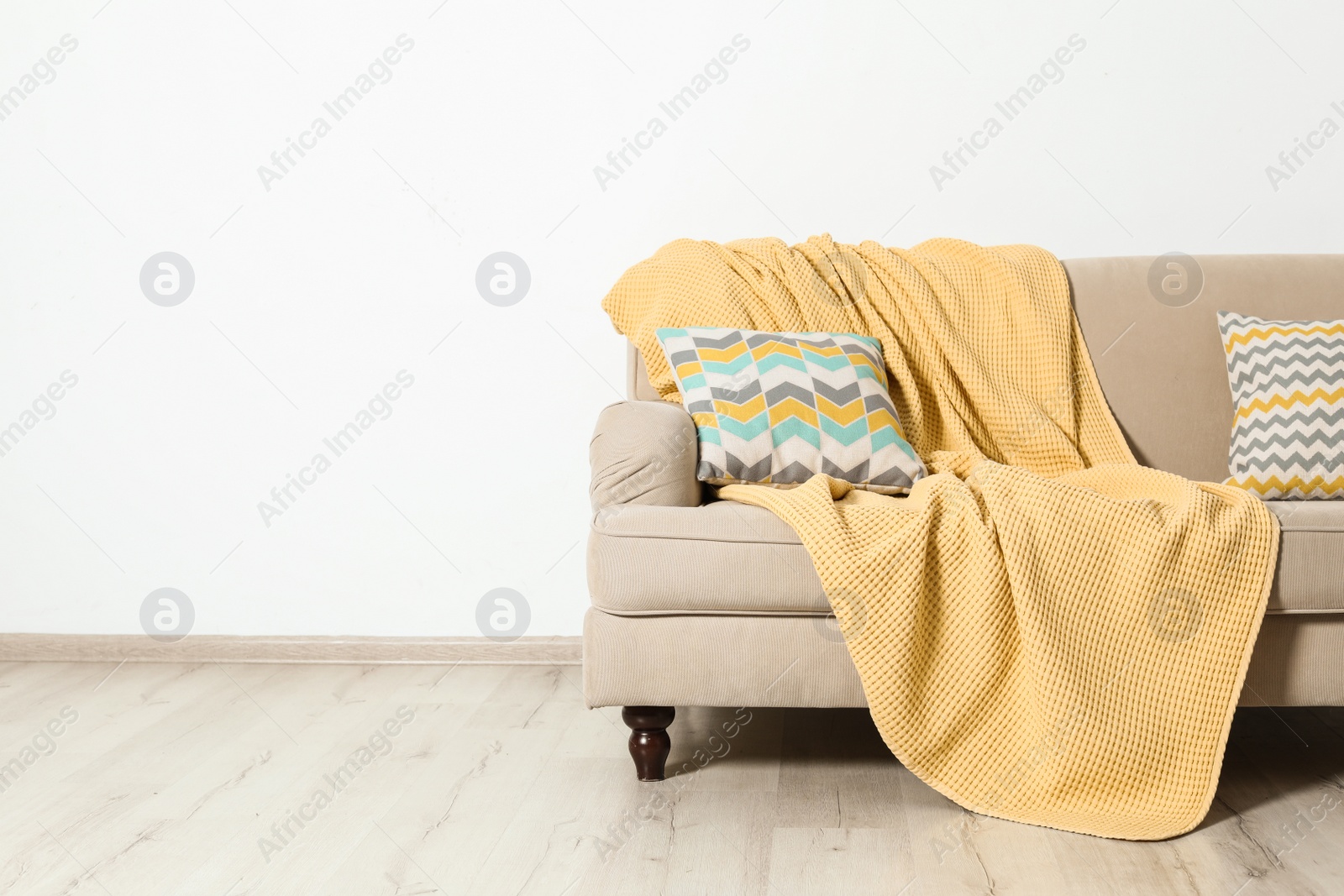 Photo of Minimalist living room interior with sofa, pillows and plaid near light wall. Space for text