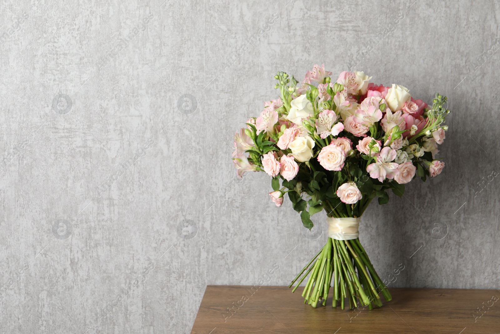 Photo of Beautiful bouquet of fresh flowers on wooden table near grey wall, space for text