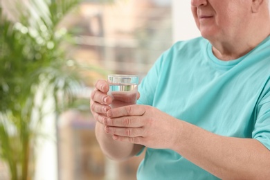 Closeup view of elderly man with glass of water in nursing home, space for text. Assisting senior generation