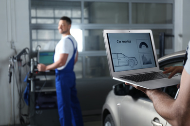 Photo of Mechanic with laptop doing car diagnostic at automobile repair shop, closeup. Space for text