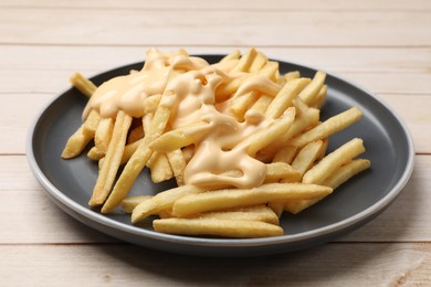 Photo of Delicious french fries with cheese sauce on wooden table, closeup