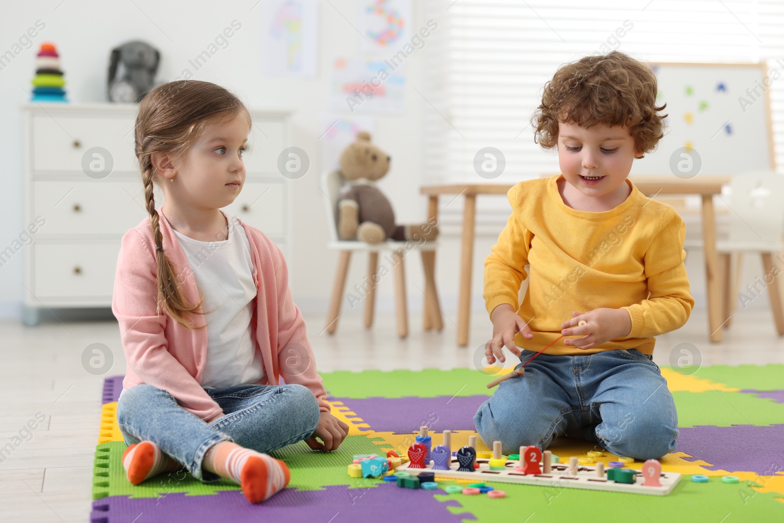 Photo of Cute little children playing with math game Fishing for Numbers on puzzle mat in kindergarten