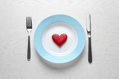 Photo of Plate with red wooden heart and cutlery on white background, flat lay. Healthy diet concept