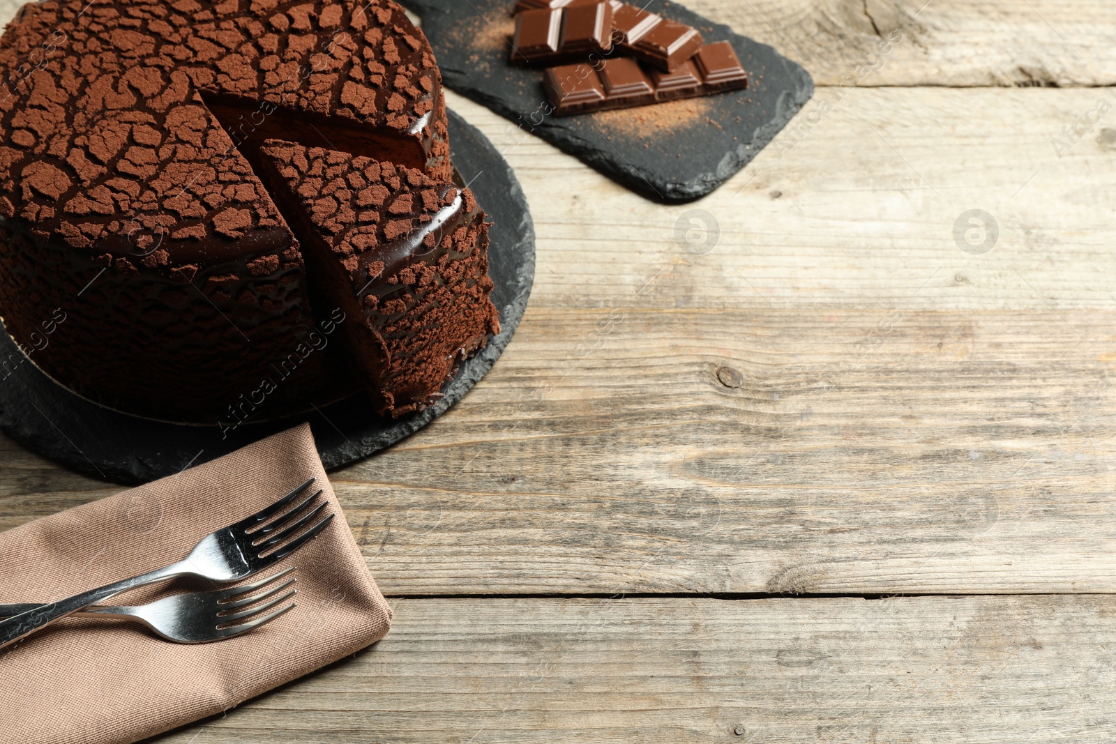 Photo of Delicious truffle cake, chocolate pieces and forks on wooden table, space for text