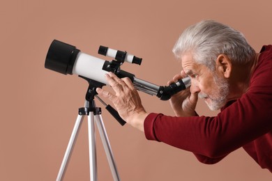 Photo of Senior astronomer looking at stars through telescope on brown background