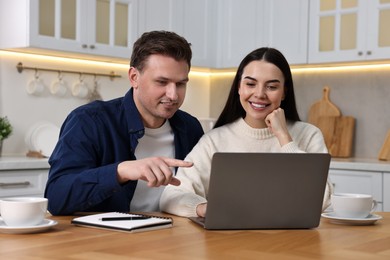 Photo of Happy couple using laptop at wooden table in kitchen