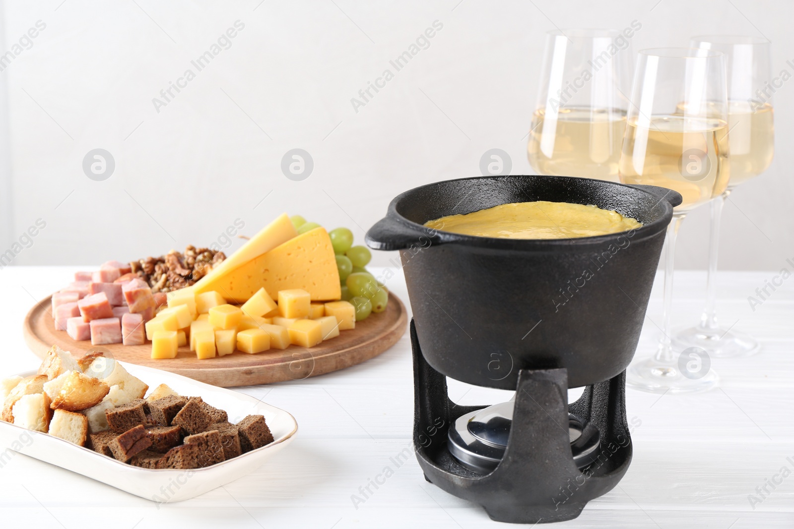 Photo of Fondue with tasty melted cheese, different products and aromatic wine in glasses on white wooden table