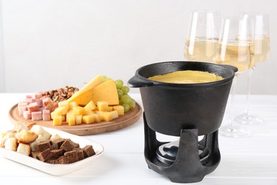 Photo of Fondue with tasty melted cheese, different products and aromatic wine in glasses on white wooden table