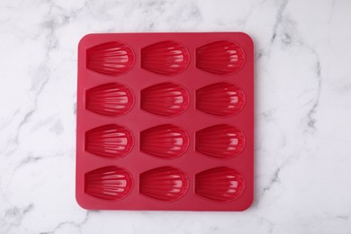 Photo of Red baking mold for madeleine cookies on white marble table, top view