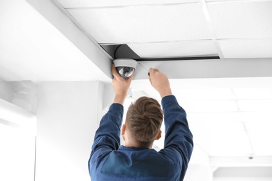 Photo of Technician installing CCTV camera on ceiling indoors