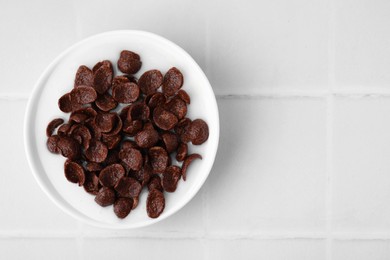 Photo of Breakfast cereal. Chocolate corn flakes and milk in bowl on white tiled table, top view. Space for text