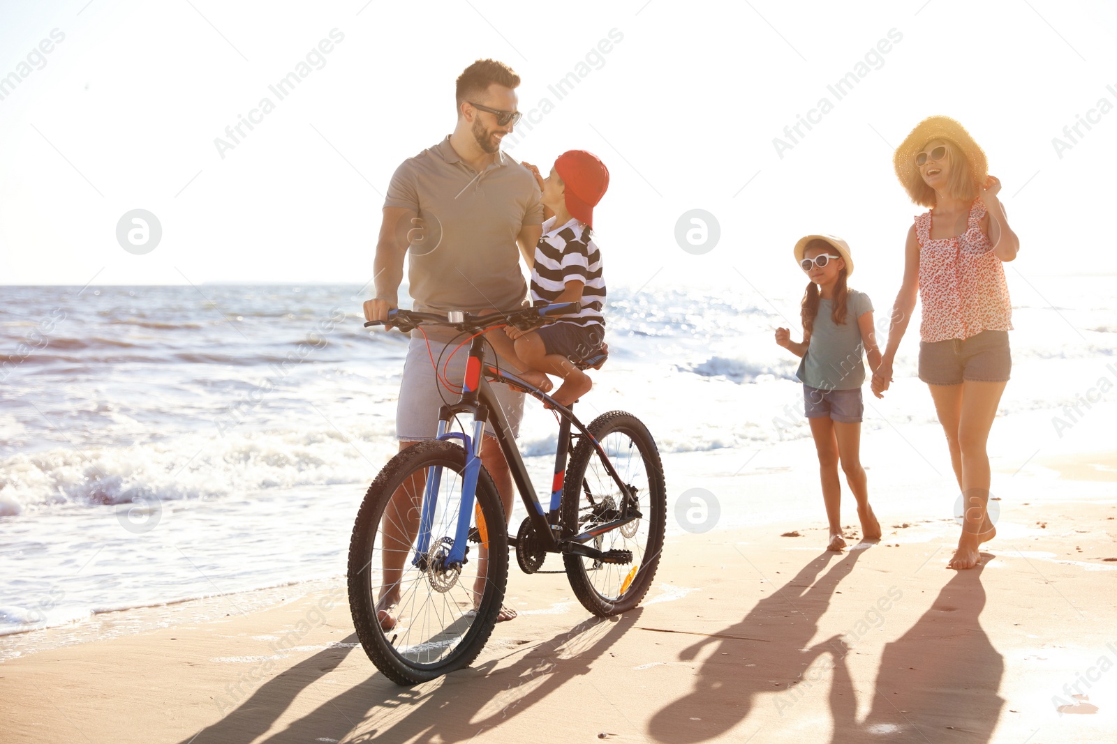 Photo of Happy family with bicycle on sandy beach near sea