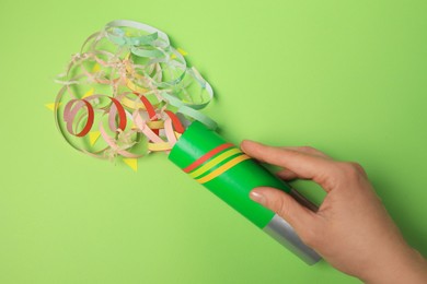 Photo of Woman holding party popper with serpentine and confetti on green background, top view