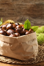 Fresh sweet edible chestnuts in paper bag on wooden table, closeup