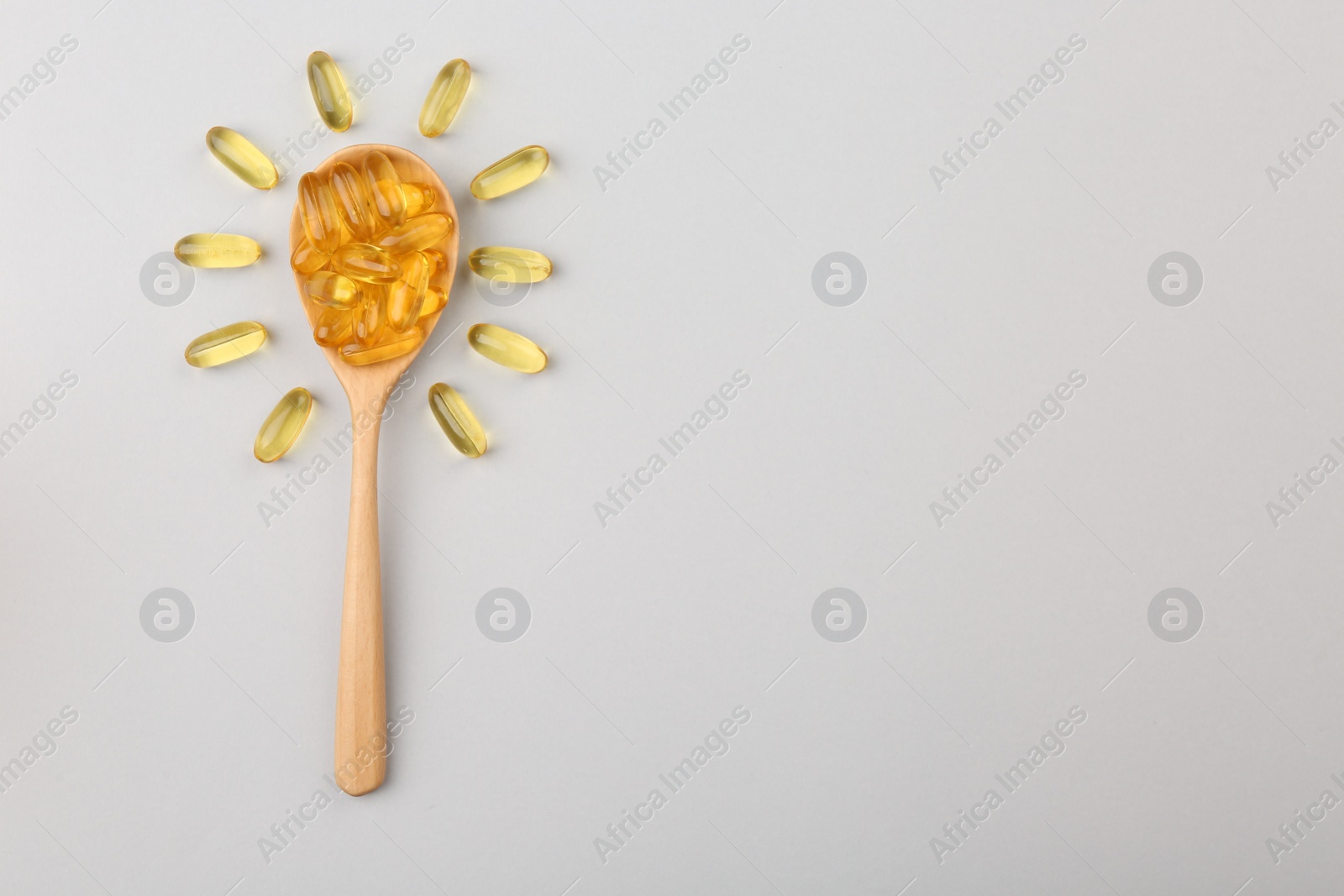 Photo of Wooden spoon with vitamin capsules on light background, top view. Space for text