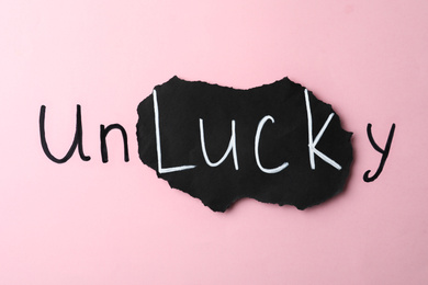Photo of Word UNLUCKY on pink background, top view