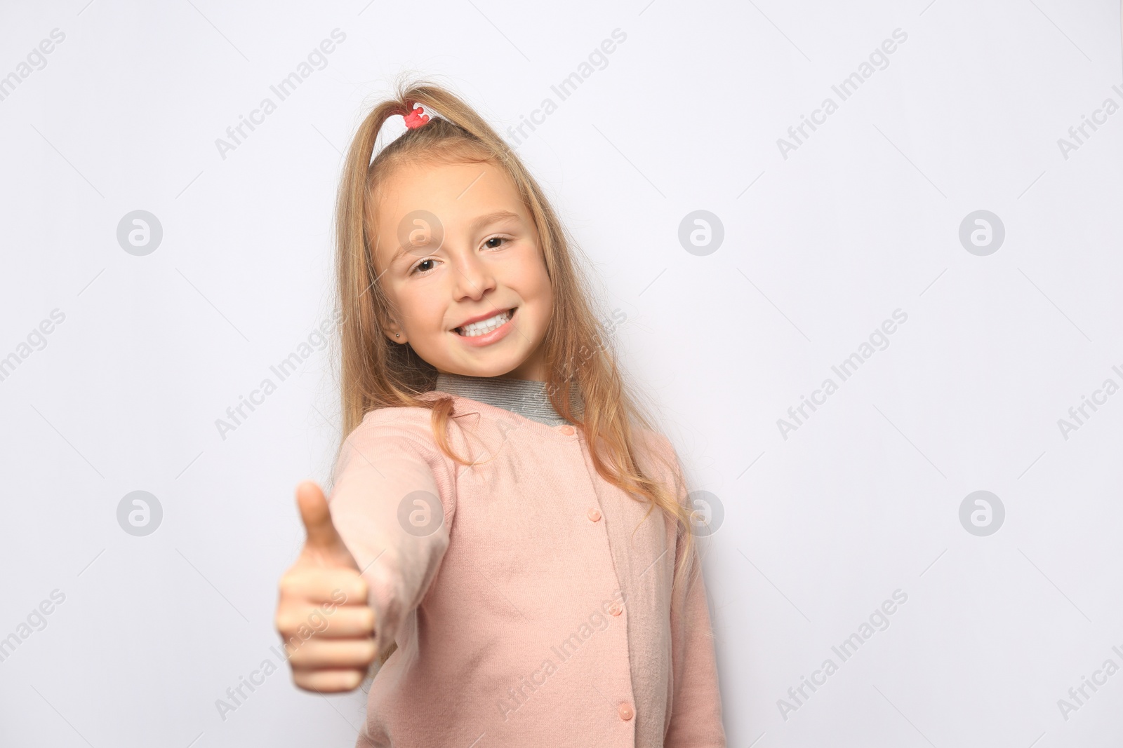 Photo of Happy little girl showing thumbs up on white background. Space for text