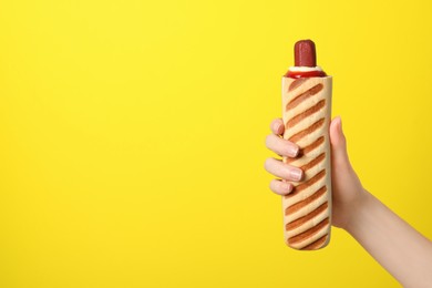 Woman holding delicious french hot dog on yellow background, closeup. Space for text