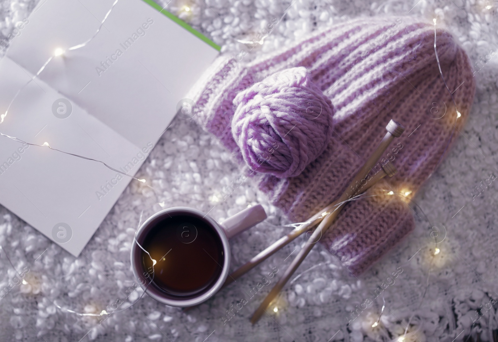 Photo of Flat lay composition with cup of hot beverage, knitting yarn and book on fuzzy rug. Winter evening