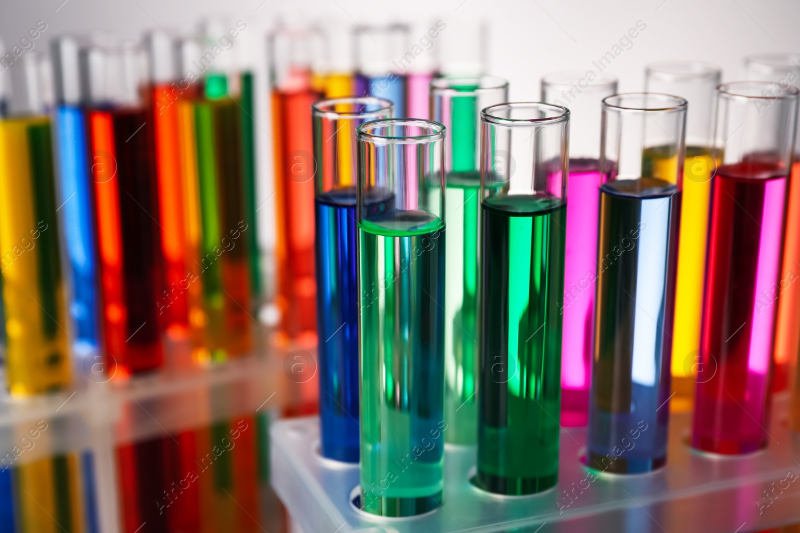 Photo of Many test tubes with colorful liquids on grey background, closeup