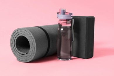 Photo of Grey exercise mat, yoga block and bottle of water on pink background