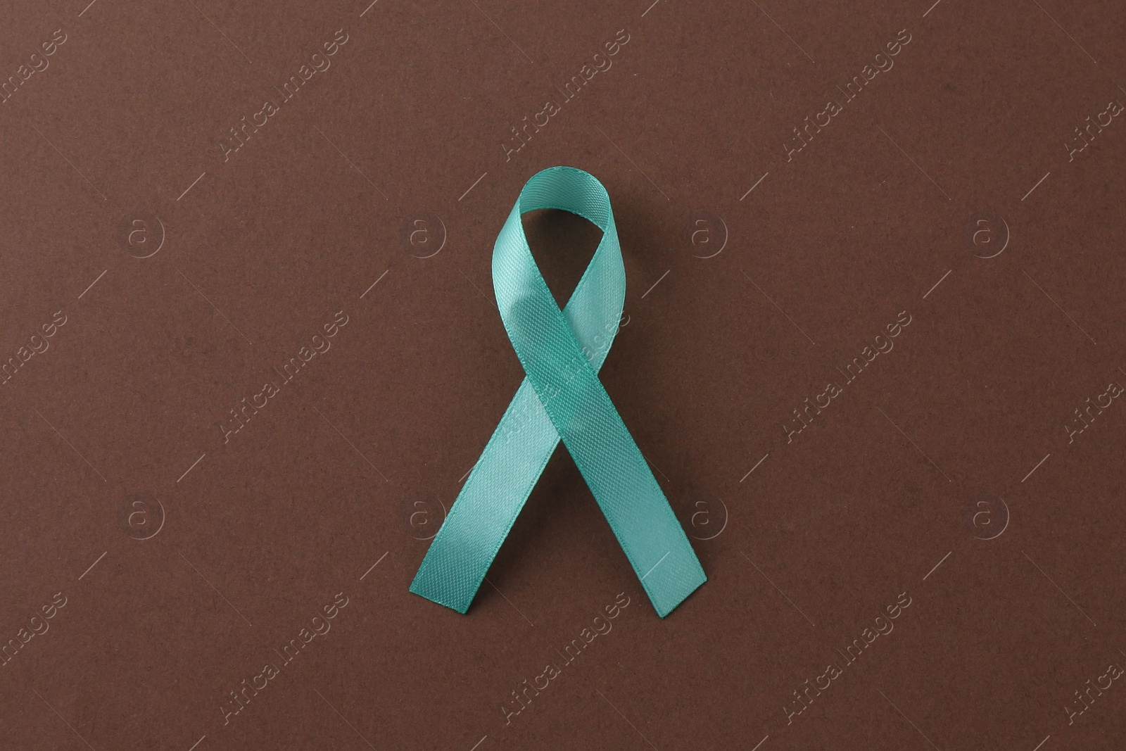 Photo of Turquoise awareness ribbon on brown background, top view