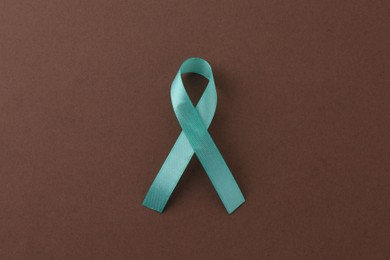 Turquoise awareness ribbon on brown background, top view