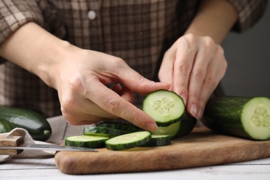 Photo of Woman putting slice of fresh cucumber onto cutting board, closeup