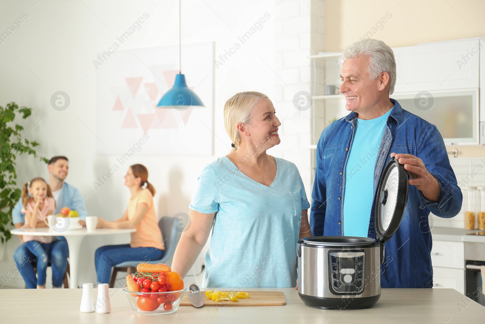 Photo of Mature couple preparing food with modern multi cooker in kitchen