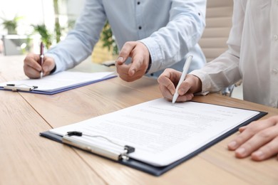 Photo of Businesspeople signing contract at table in office, closeup