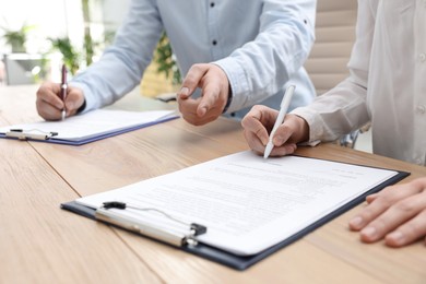 Businesspeople signing contract at table in office, closeup