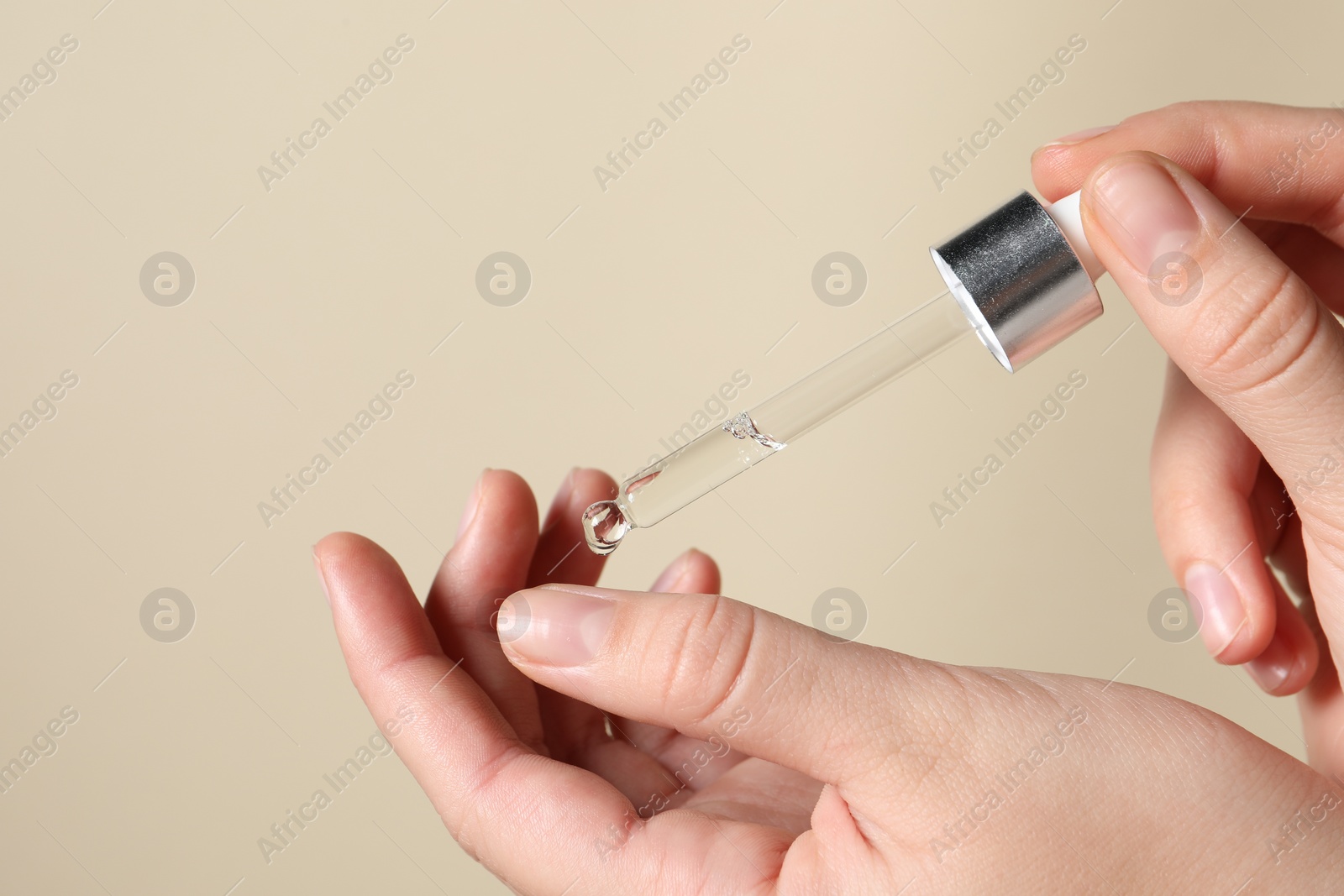 Photo of Woman applying cosmetic serum onto finger on beige background, closeup. Space for text