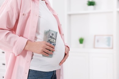 Surrogate mother. Pregnant woman with dollar banknotes indoors, closeup. Space for text