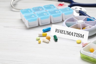 Card with word Rheumatism and pills on white wooden table, space for text