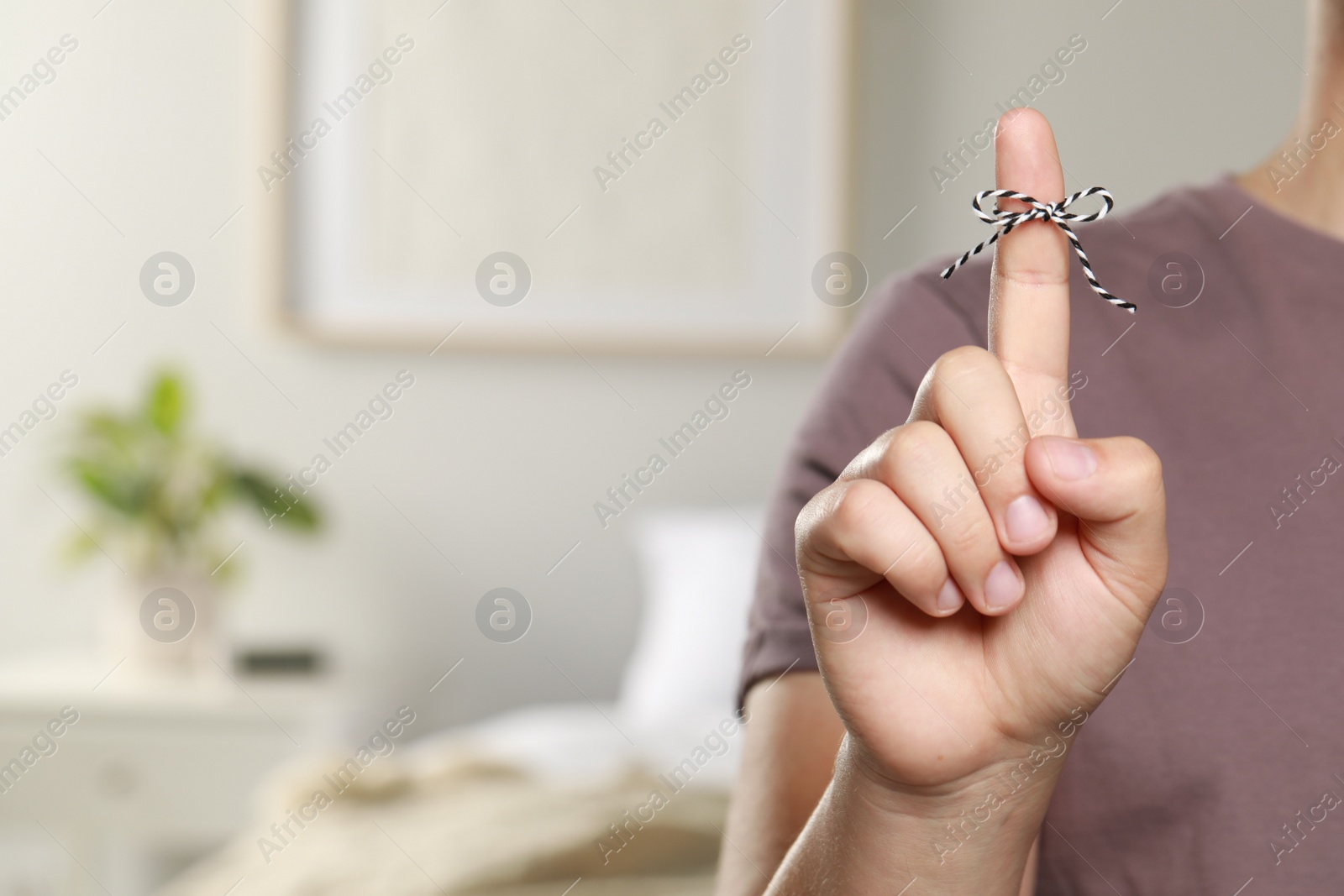 Photo of Man showing index finger with tied bow as reminder indoors, closeup. Space for text