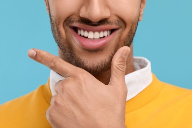 Photo of Smiling man with healthy clean teeth on light blue background, closeup