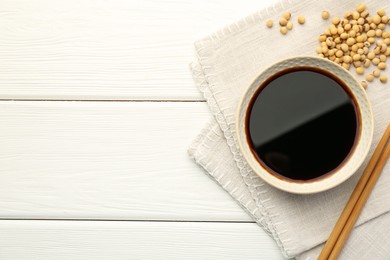 Photo of Tasty soy sauce in bowl, chopsticks and soybeans on white wooden table, top view. Space for text