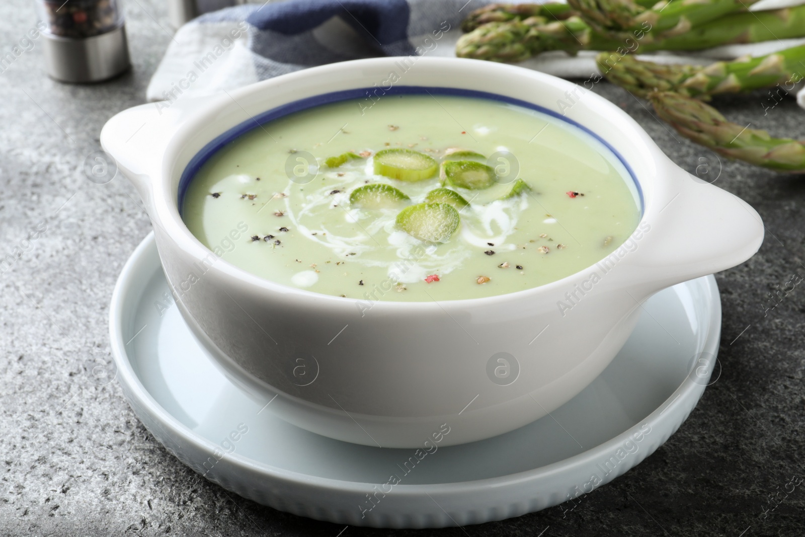 Photo of Bowl of delicious asparagus soup on grey table