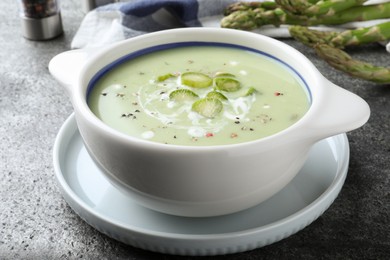 Bowl of delicious asparagus soup on grey table