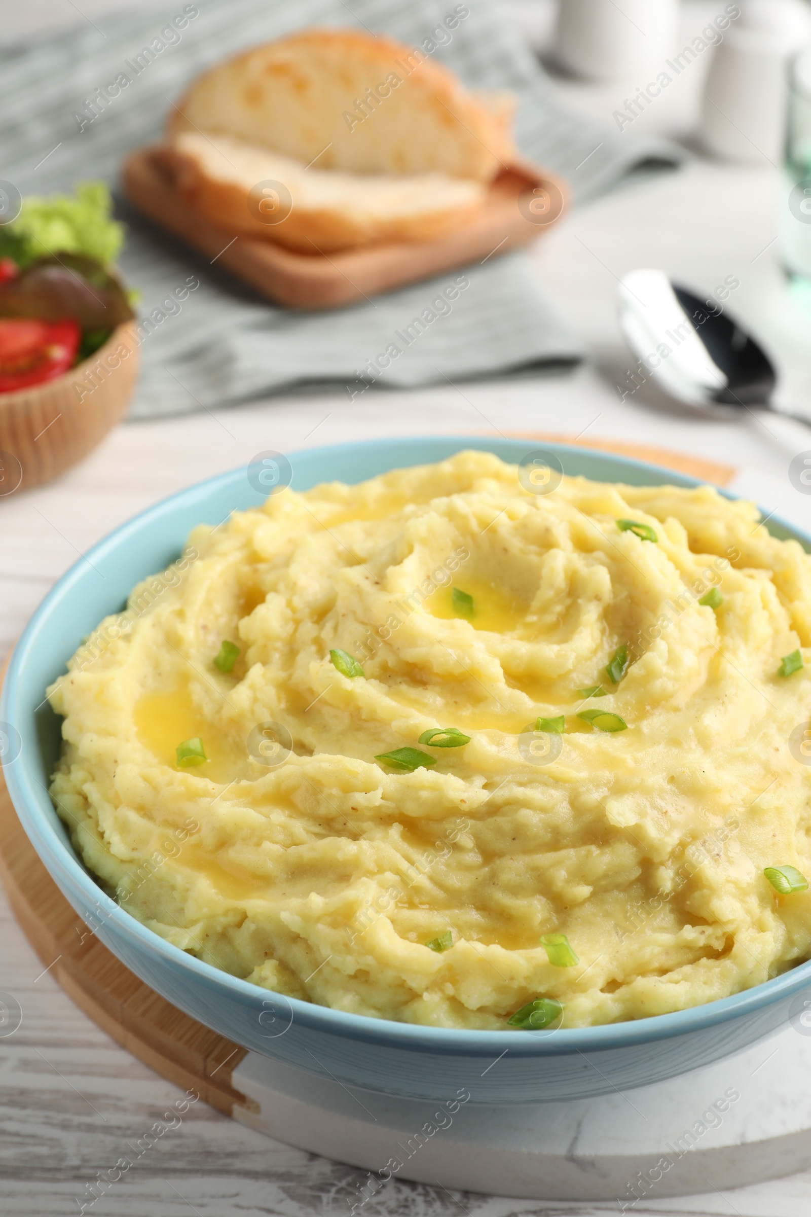 Photo of Bowl of tasty mashed potatoes with onion served on white wooden table, closeup