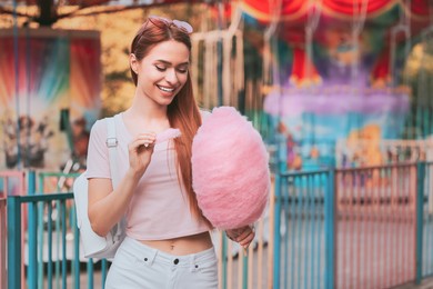 Beautiful woman eating cotton candy at funfair. Space for text