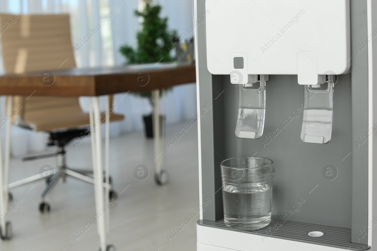 Photo of Modern water cooler with glass in office, closeup. Space for text