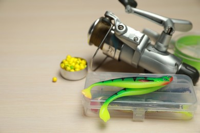 Photo of Different fishing baits and reel with line on light wooden table, closeup. Space for text