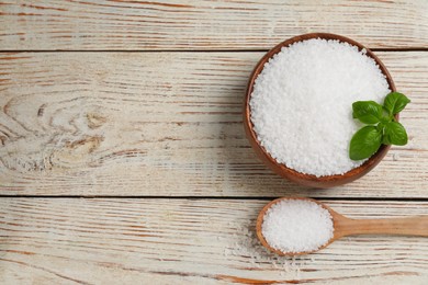 Bowl and spoon with natural sea salt on white wooden table, flat lay. Space for text